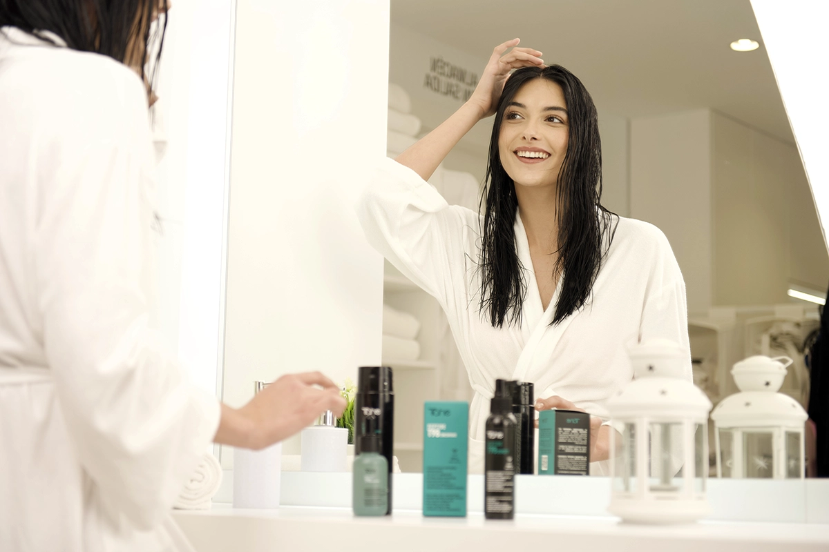 Mujer frente al espejo aplicando tratamiento capilar con productos cosméticos