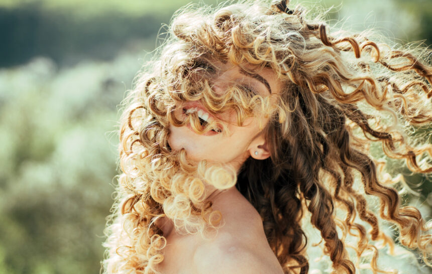 Mujer con rizos rubios al aire libre, sonriendo con el cabello en movimiento