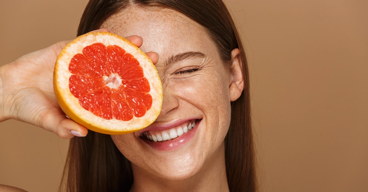Mujer sonriente con una rodaja de pomelo rosado frente al ojo