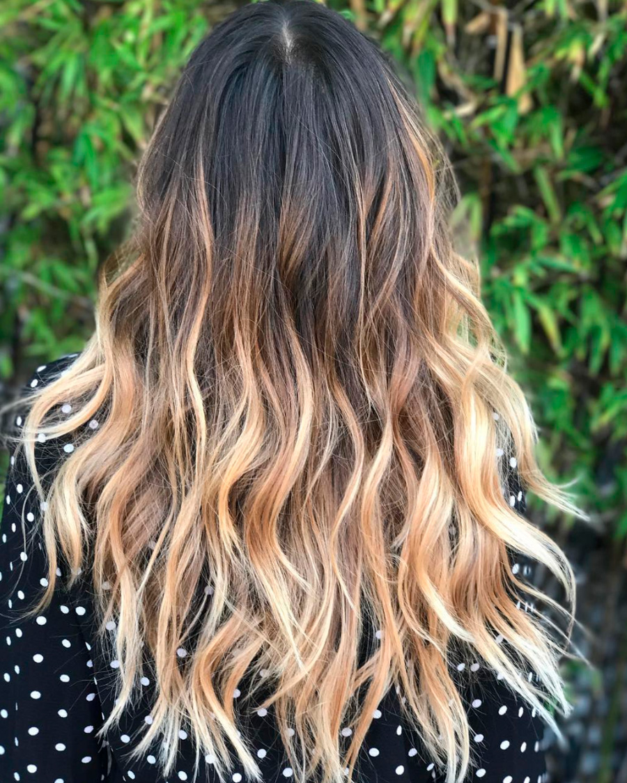 Mechas californianas en rubio beige fundido sobre cabello largo y oscuro con ondas sueltas