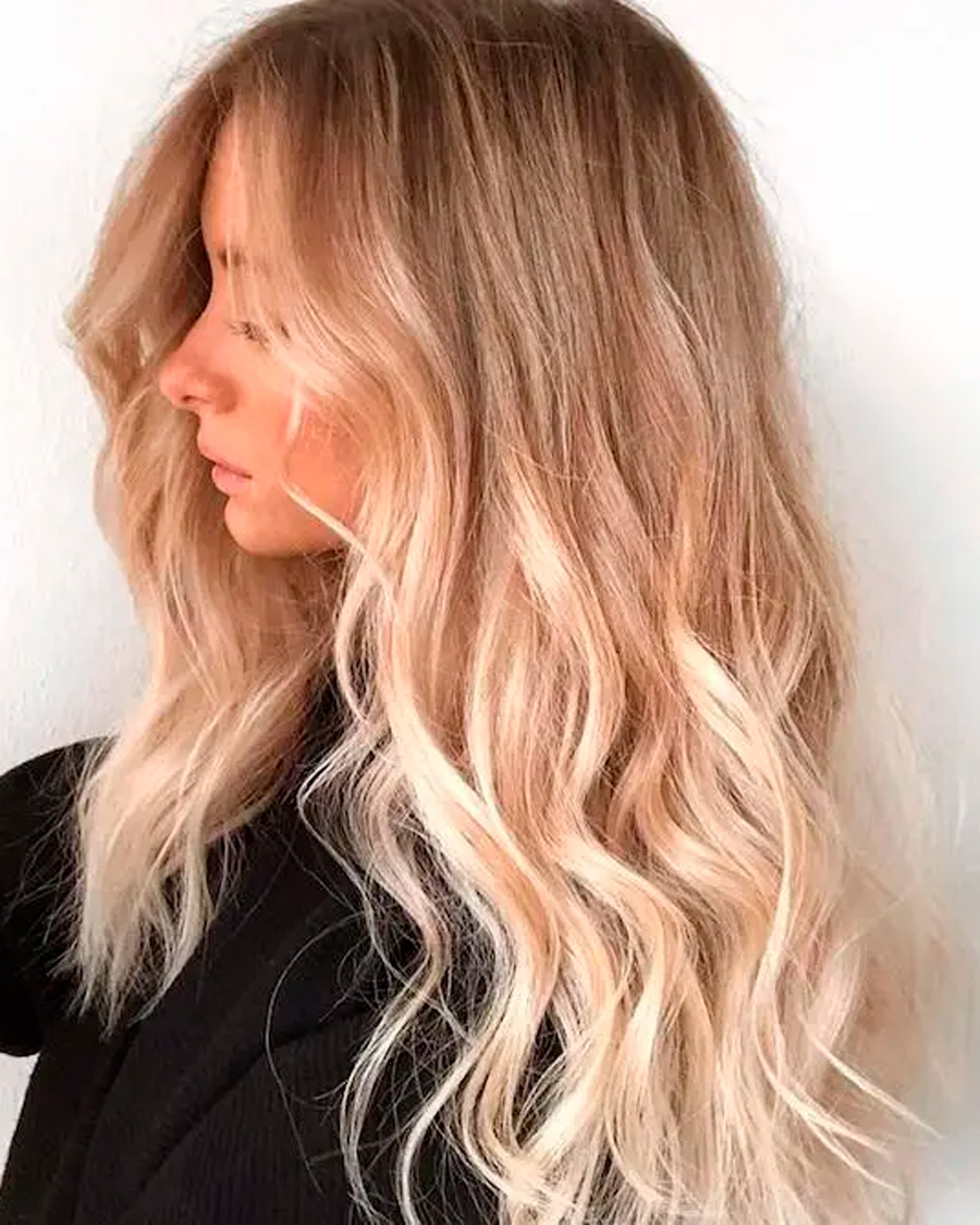Mechas californianas rubias en tonos vainilla frío con acabado pulido en cabello largo ondulado