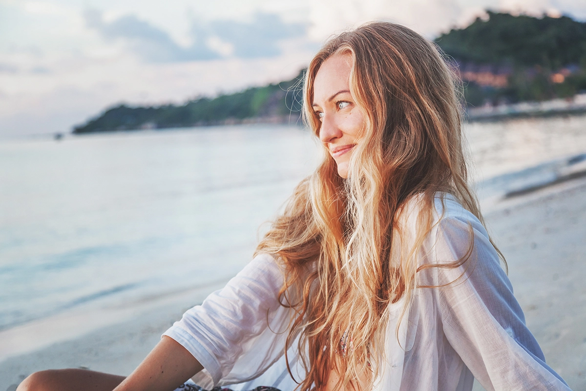 Mujer en la playa con el cabello rubio hidratado y saludable en verano.