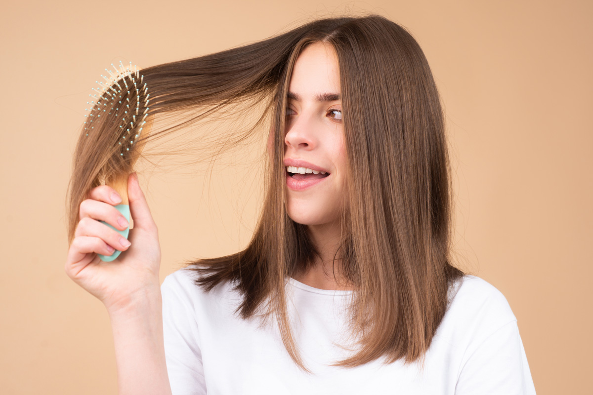 Mujer revisando su cabello con gesto curioso mientras sujeta un mechón.