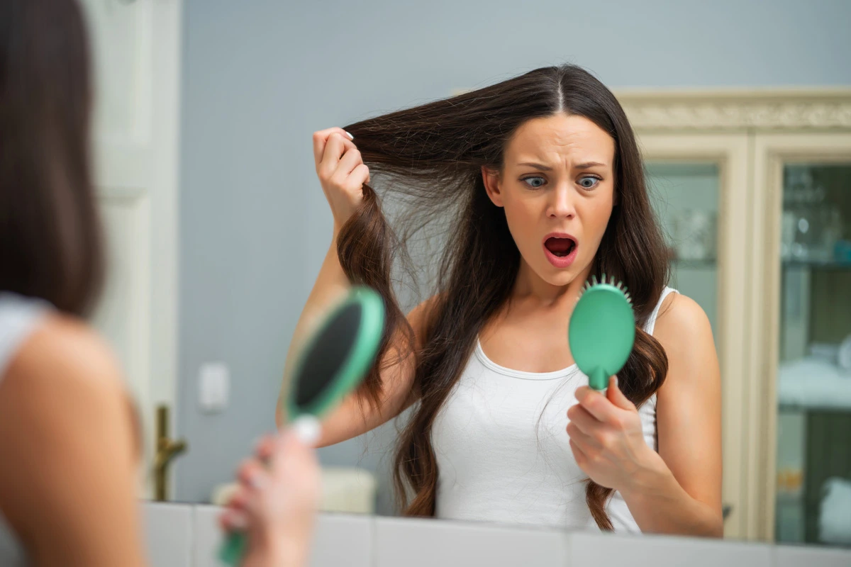 Mujer sorprendida al ver la caída de su cabello mientras se peina frente al espejo